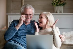 elderly couple sitting at laptop on couch and feeling happy about their internet service