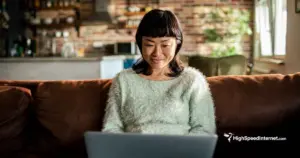 asian woman happily using computer sitting on couch