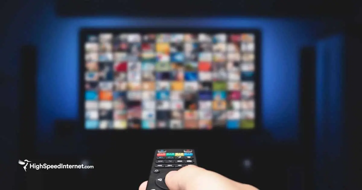 person pointing remote at tv with streaming services in a darkly lit room
