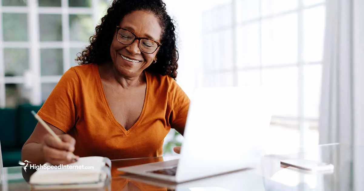 Woman smiling writing in a notepad next to an open laptop