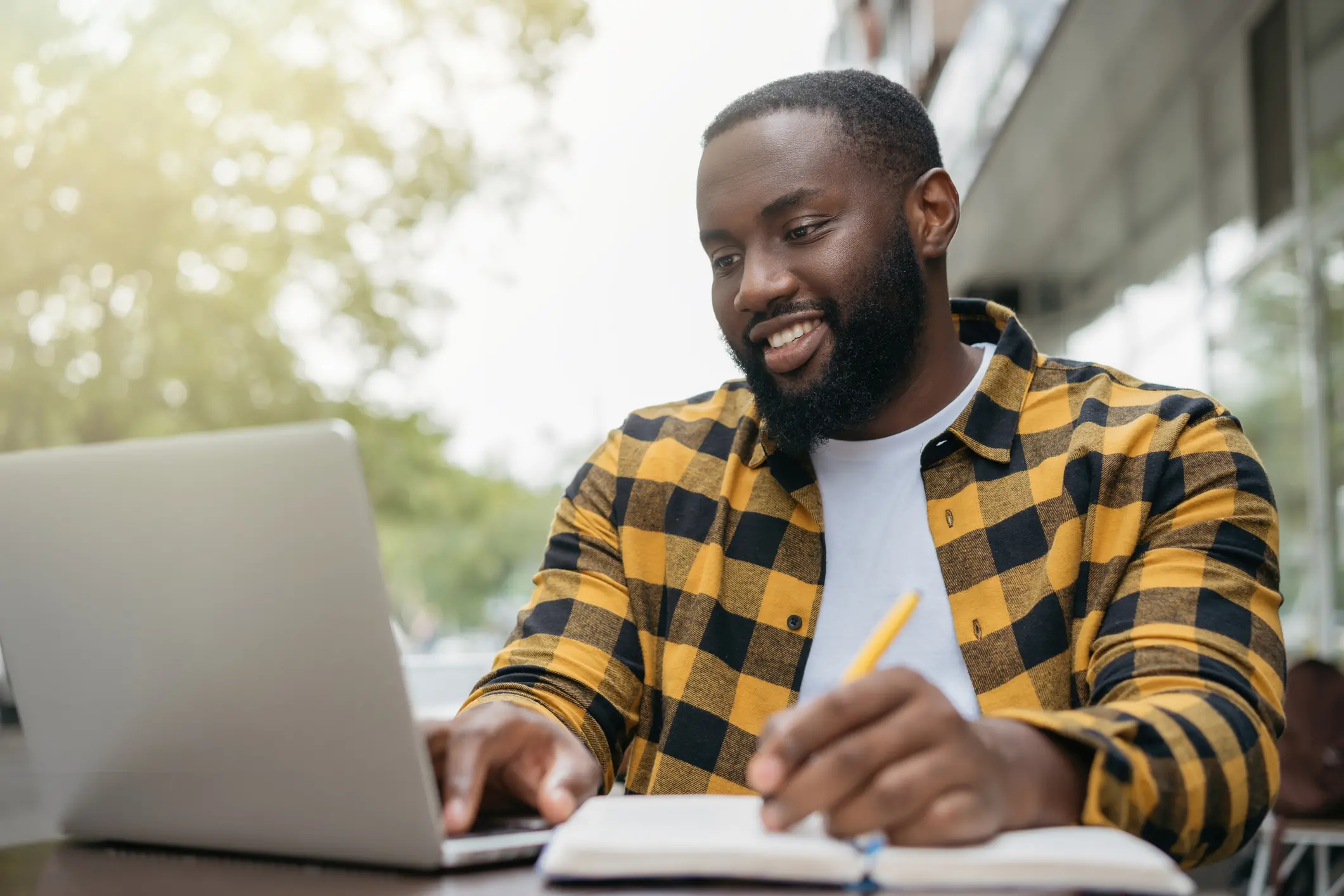 African American man using laptop computer, taking notes, planning start up, working online. Portrait of happy student studying, learning languages, online education concept