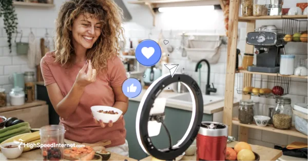 photo of woman blogging in her kitchen with phone set-up on a tripod with simplified social media illustrations: like, love, and share