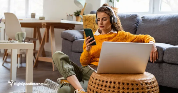 Woman sitting at home looking at phone and laptop