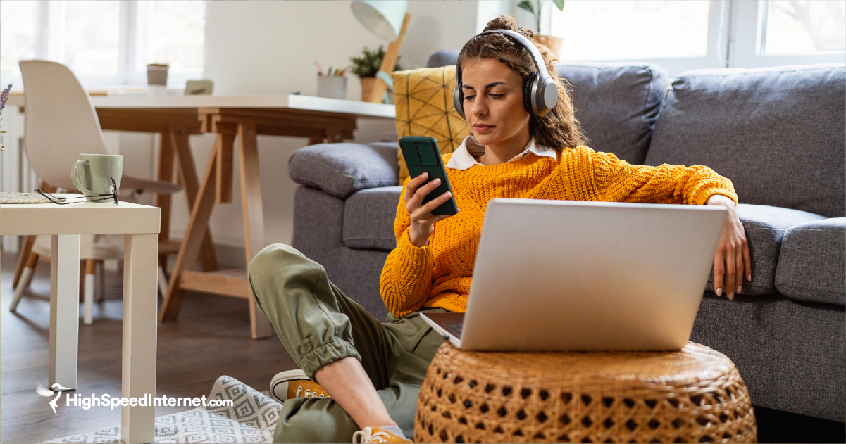 Woman sitting at home looking at phone and laptop