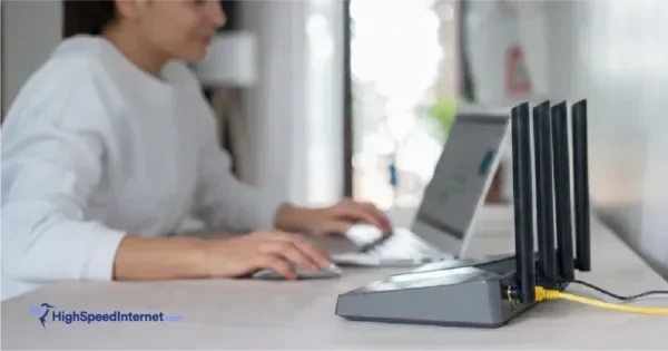 Close-up of a modern Wi-Fi router on a desk with a blurred woman working on a laptop in the background